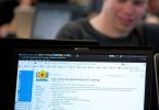 A programmer reviewing lines of code on a large monitor in a dim office.