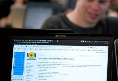 A programmer reviewing lines of code on a large monitor in a dim office.