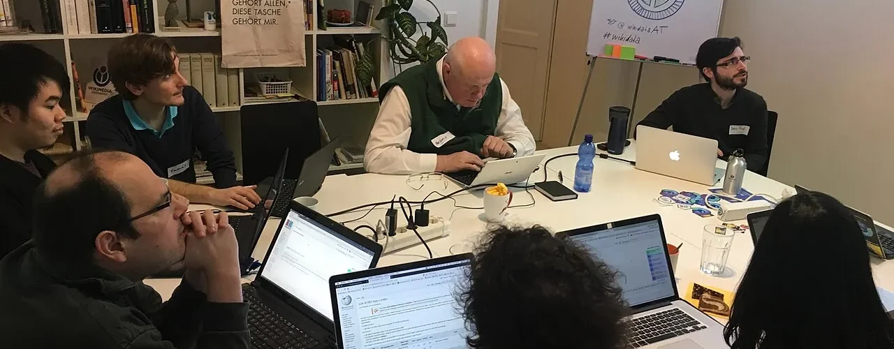 People collaborating on laptops around a shared workshop table.
