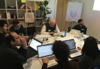 People collaborating on laptops around a shared workshop table.