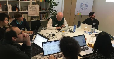 People collaborating on laptops around a shared workshop table.