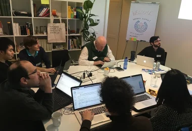 People collaborating on laptops around a shared workshop table.