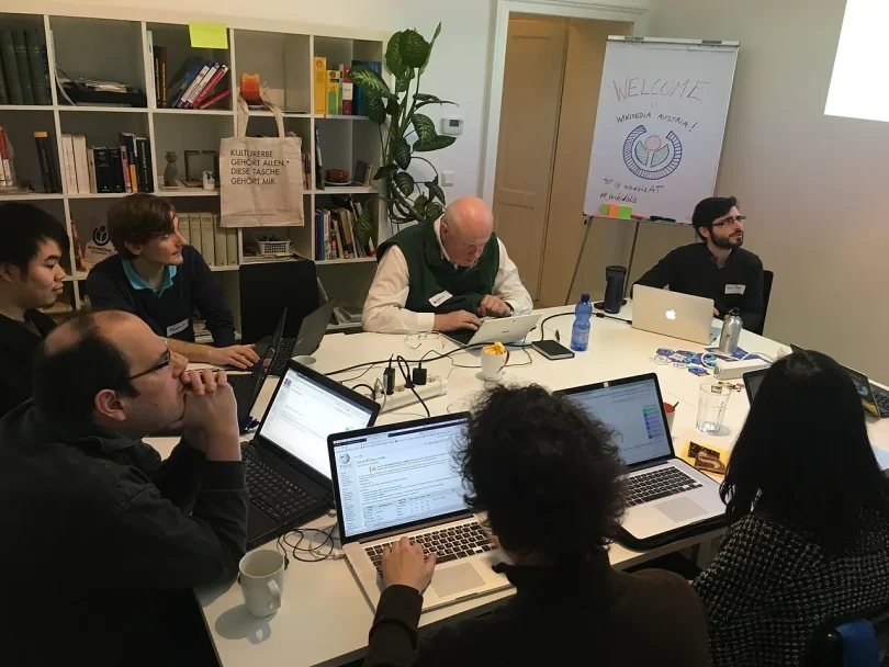 People collaborating on laptops around a shared workshop table.